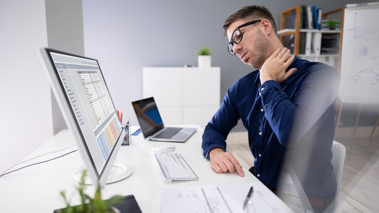 a guy holding his back as he is having pain sitting at his desk 